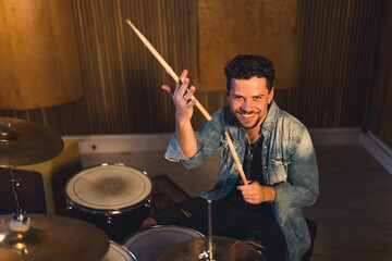 Caucasian middle-aged bearded drummer man holds wooden sticks, sits next to percussion and smiles...