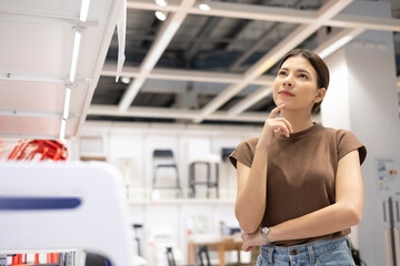 Young beautiful woman choosing the right chair furniture for her house at showroom. Female looking and thinking near lot of armchair at furniture store hall. Buying various item for new house