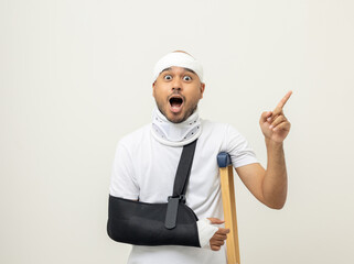Shocked face man broken arm and leg pointing finger to blank space. Man put on plaster cast splint...