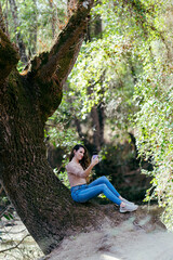 Chica joven con pelo largo ondulado en sendero verde con smartphone interactuando y haciendo fotos 