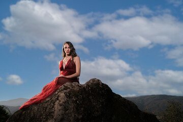 Fototapeta na wymiar Chica joven con vestido rojo en zona boscosa y castillo medieval posando
