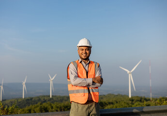 Engineer India man working at windmill farm Generating electricity clean energy. Wind turbine farm generator by alternative green energy. Asian engineer checking control electric power