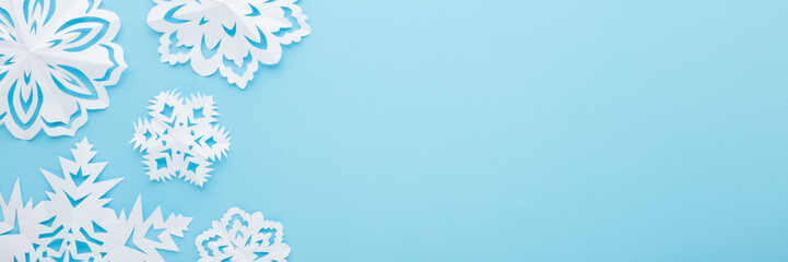 White snowflake shapes created from paper on light blue table background. Pastel color. Closeup....