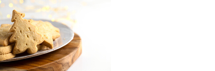Christmas cookies treat background for banner. Different festive shape and Christmas tree shape Scottish shortbread on the white plate with bokeh. Copy space