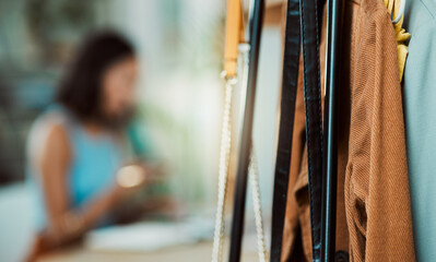 Fashionable clothes, wardrobe display and boutique collection hanging on store rail with designer, stylist and woman working in the background. Closeup of trendy clothing design in a creative startup