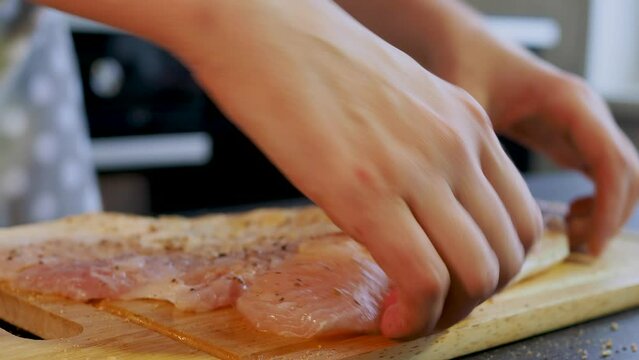 A woman in an apron cooks at home in the kitchen. Fillet of white fish on a board, salt and pepper, close-up