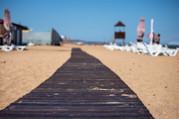 Wooden beach path made of dark boards on light sand on the sea beach, selected focus.