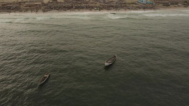 A dron reveal shot of the MAuritanian coast, starting on three anchored boats, and moving up the camera revealing the Port P&egrave;che view, with the buildings and the boats on the beach.