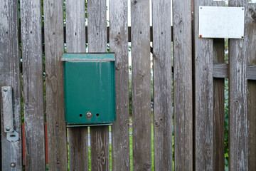 Mailbox, green on a wooden gate, a frame hangs on the fence nearby.