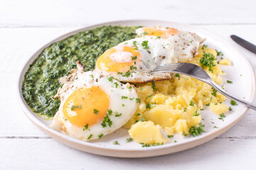 Creamed spinach with fried eggs, sunny side up and boiled potatoes on a plate isolated on white background