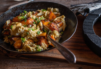 Roasted sweet potatoes with scrambled eggs, chives and parsley in a rustic pan. Healthy muscle building fitness meal