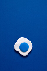 Gummy candy fried egg with blue yolks on a blue background. Minimal abstract creative concept. Modeling clay.