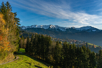 Panorama mit dem herbstlichen Dornbirn Kehlegg und der frisch verschneiten Gebirgskette First im Hintergrund. blauer Himmel mit föhnigen Schleierwolken.