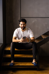 Business man sitting indoors on stairs near flower pots with plants and use phone.