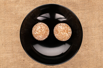 two sweet tasty gingerbread cookies in a black ceramic plate on a jute cloth, macro, top view.