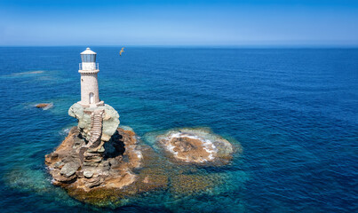 The Tourlitis lighthouse on a steep rock in calm, blue sea with a seagull, Andros island, Cyclades,...