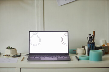 Close up of open laptop with jewelry designs at screen in minimal studio interior, copy space