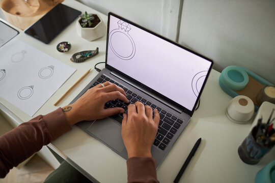 Top view closeup of creative artist typing at laptop keyboard and designing jewelry, copy space