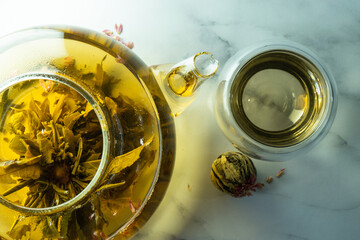 Chinese blooming tea. A glass teapot with a blooming tea flower on a white table. a cup of Chinese blooming tea and tea balls. Selective focus.