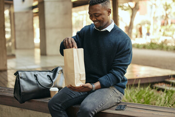 Office employee with a coffee, a paper sandwich bag and a smile, on a bench for a break from his...