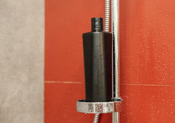 A black plastic bottle for detergent, tonic, conditioner, soap or shampoo in the bathroom near the red wall in drops of water. Natural organic cosmetics, packaging with an empty label.