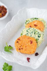 Assorted, salted butter with parsley and butter with paprika and salt, cut into circles, on a white rectangular plate, on a light concrete background. Types of butter for serving dishes.