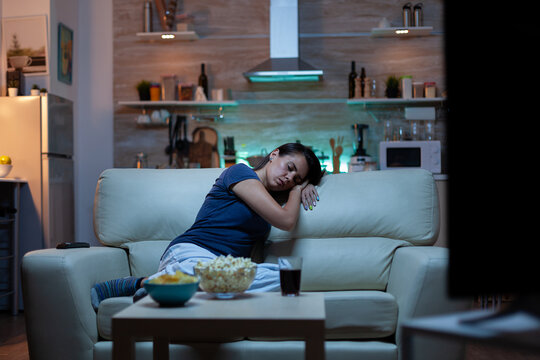 Woman Falling Asleep On Sofa In Front TV. Tired Exhausted Lonely Sleepy Lady In Pajamas Sleeping In Front Of Television Sitting On Cozy Couch In Living Room, Closing Eyes While Watching Movie At Night