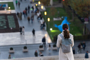 A woman with a backpack stands in a city park.