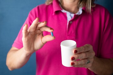 Woman holds a container with blue pills in her hand against a blue background - Medical supplies