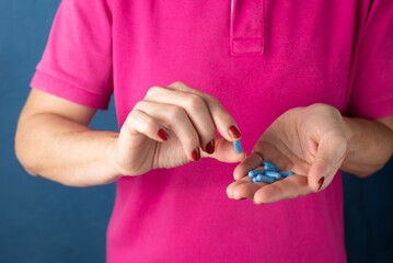 Woman holding blue pills in her hand against a blue background - Medical supplies concept