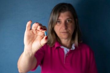 Woman holding blue pills in her hand against a blue background - Medical supplies concept