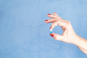 Female hand holding a pill against a blue background - Medical supplies concept