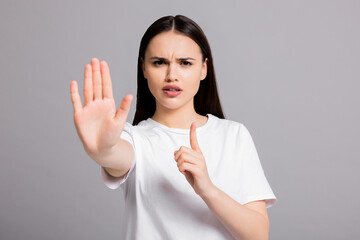 Angry young woman in white casual basic t-shirt standing on grey background isolated shwoing stop gesture at camera.