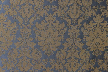 Golden-blue fabric with ornament of flowers and leaves as background.