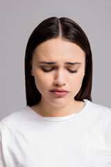 Close up shot selective focus autumn depressive mood expressions sad cried young woman standing on grey background in studio isolated wearing white t-shirt looking down desperation.