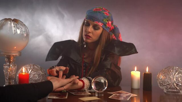 Young generic witch performing fortunetelling prediction using hand paw of her client, gypsy creating spiritual bond with afterlife, talking with ghost and predicting future or telling about the past