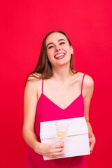 Funny young woman with a glass of champagne and a gift for the New Year on a red background