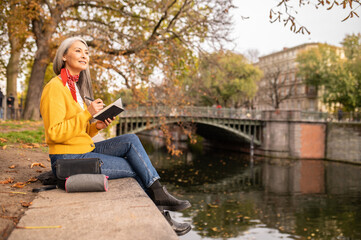 Woman sitting on the river bank, making notes and looking inspired