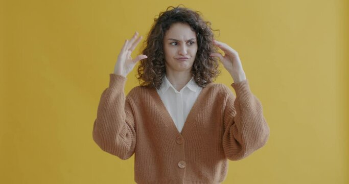 Portrait of cute young woman tired of blabbing showing bla bla bla hand gesture and looking at camera on yellow background. People and expression concept.