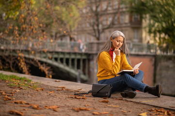 Mature woman sitting on the river bank and drawing in album