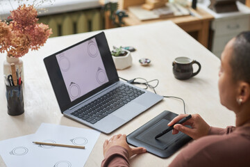 Closeup of female artist using graphic tablet while designing jewelry rings in studio