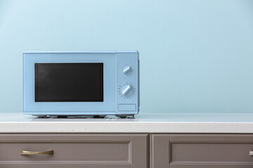 Modern microwave oven on counter near light blue wall
