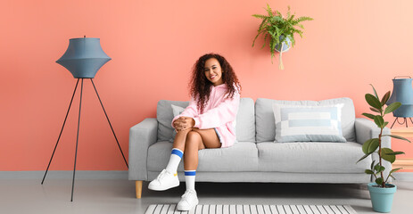 Young woman relaxing on comfortable sofa near pink wall in room