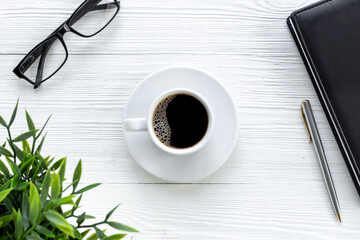 Office table with cup of hot black coffee and notebook