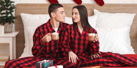 Obraz premium Young couple with cups of hot chocolate in bedroom on Christmas eve