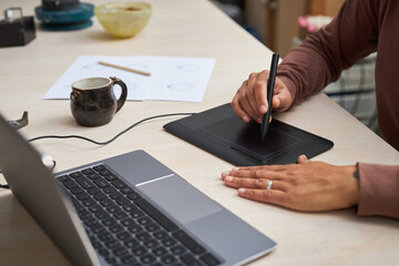 Closeup of unrecognizable black woman working on new designs in studio and using pen tablet