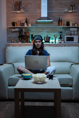 Woman freelancer in pijamas working late at night on laptop in front tv. Happy person in pijamas...