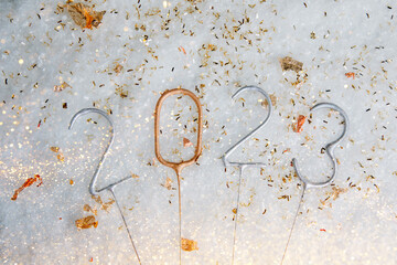 New Year, Christmas background. Candle numbers 2023 in silver and golden colours on a white snow background with confetti. Flat lay