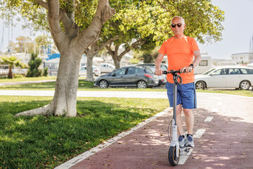 Uomo anziano con una maglia arancione corre sul suo monopattino elettrico  in una pista ciclabile  