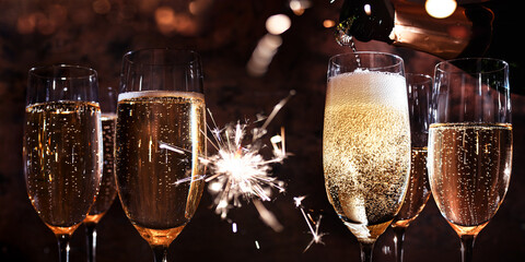 New year toasting with champagne and sparklers on dark background. Atmospheric horizontal close-up...